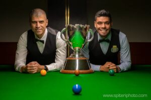 Steve Mifsud and Vinnie Calabrese lean on the table with the Australian Open trophy between them which is also on the table.