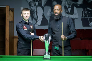 Antoni Kowalski and Rory McLeod shake hands before the final by the table. The trophy is on the table in between them in front of them.