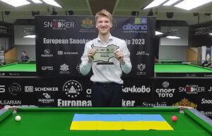 Iulian Bokio poses with the trophy and behind a Ukrainian flag which is on the snooker table.