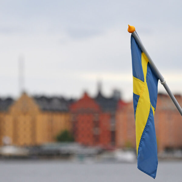 A picture of Stockholm behind the water and with the Swedish flag in the forefront of image.