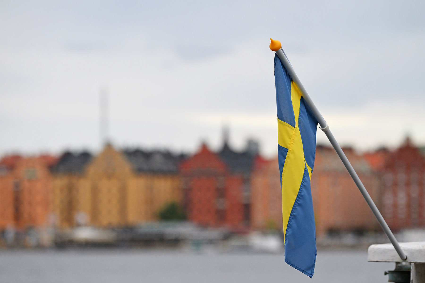 A picture of Stockholm behind the water and with the Swedish flag in the forefront of image.