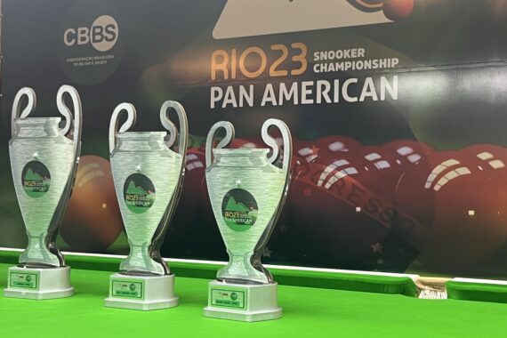 The 2023 Pan American Snooker Championship trophies are lined up on the table in front of the a big tournament wall poster.